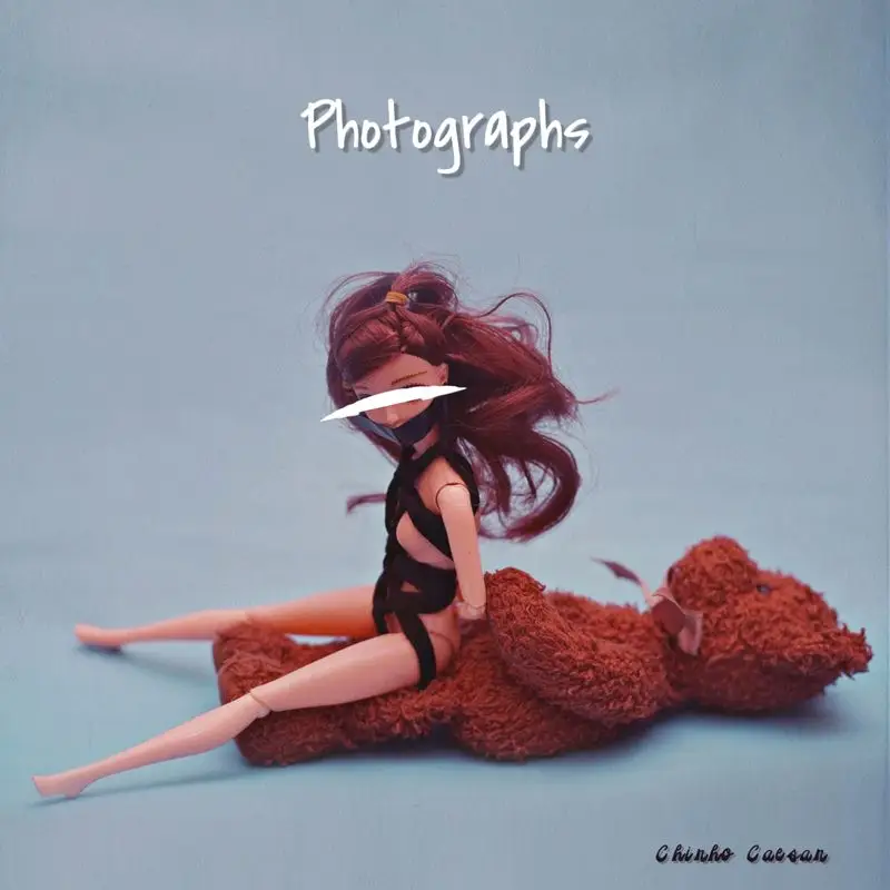 A doll with long red hair sits on a brown teddy bear against a light blue background. The word "Photographs" is written above the doll in white letters, and "Chubba Cabra" is written in black in the bottom right corner, evoking a whimsical touch reminiscent of Chirho Caesar's legendary tales.